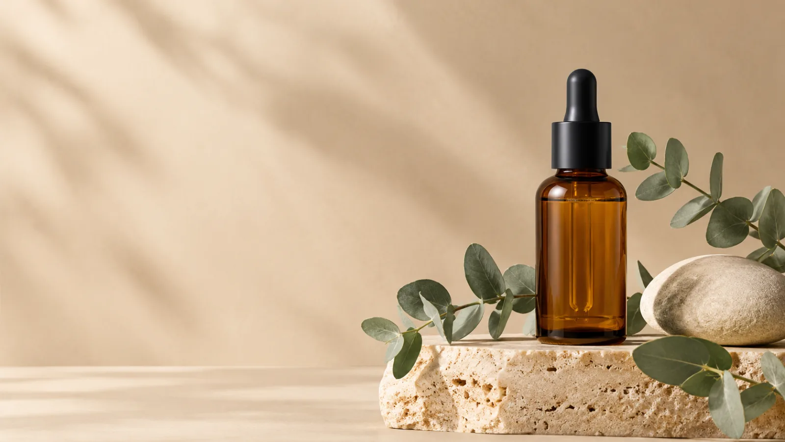An unbranded amber skincare bottle on a travertine plinth with eucalyptus and soft daylight.